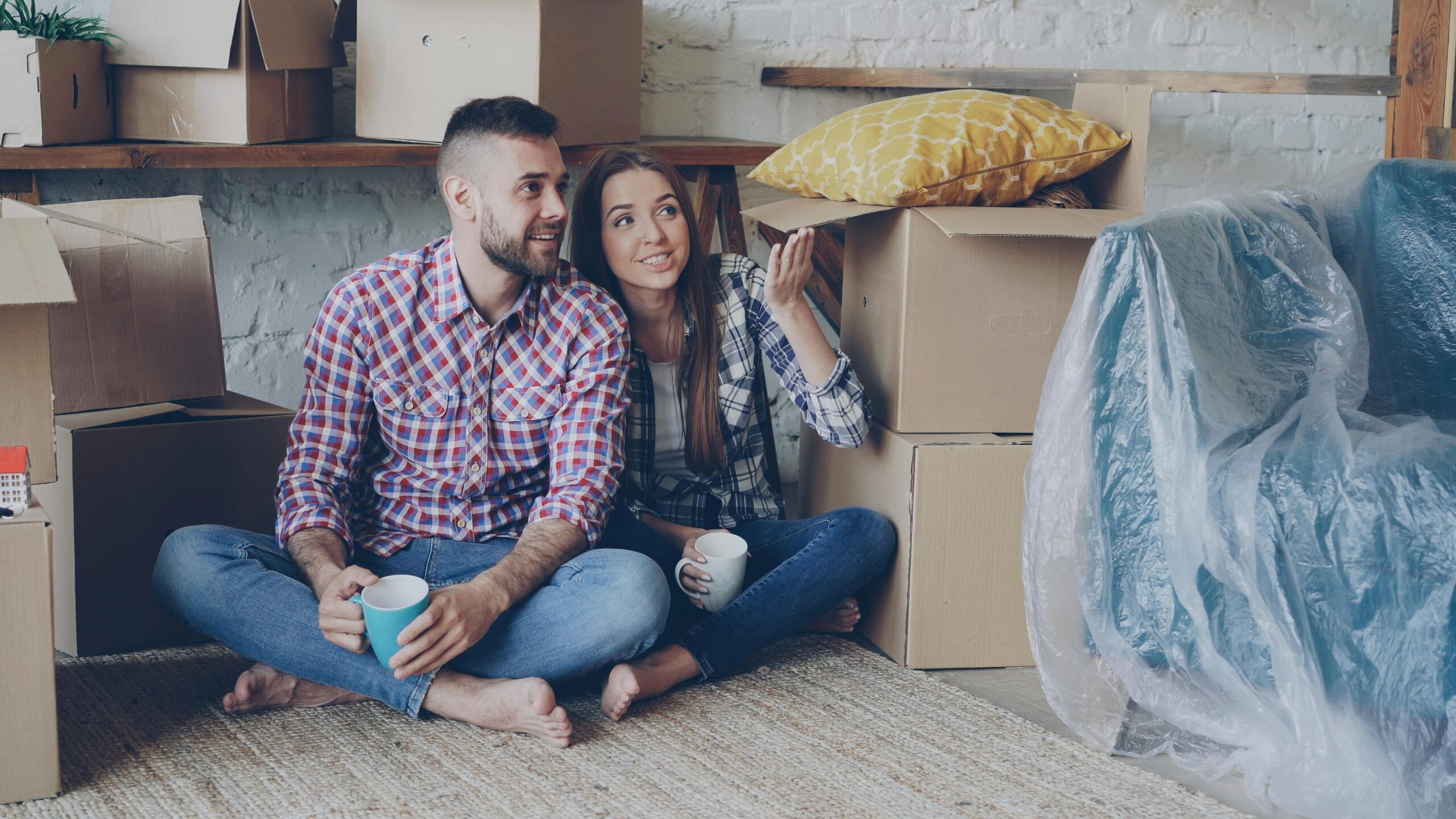 Couple sitting with coffee among moving boxes, planning their new home decor.